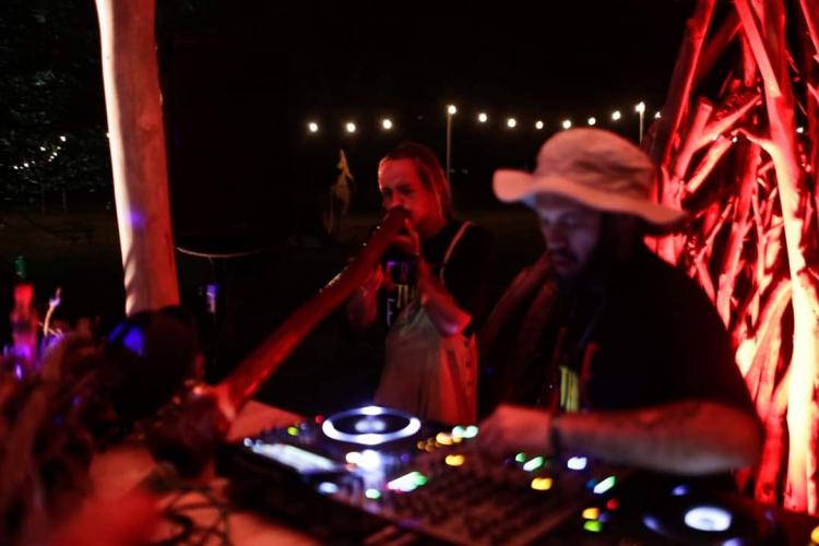 The two members of Dreamtimin jamming on stage. One DJing with a bucket hat on the other in overalls and a black t-shirt playing the didgeridoo.