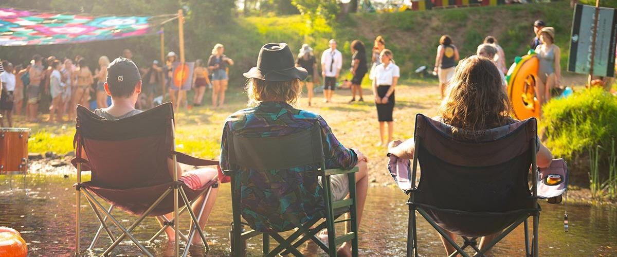 Three festival goers sitting in camping chairs in a creek at a previous instalment of Jungle Love Festival
